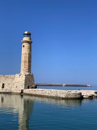 Lighthouse by sea against clear sky