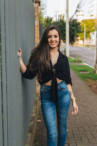 Portrait of smiling young woman standing by fence