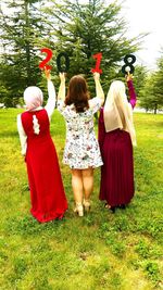 Rear view of women with arms raised holding numbers while standing on field at park