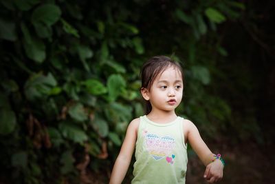 Cute girl looking away while standing against plants in park