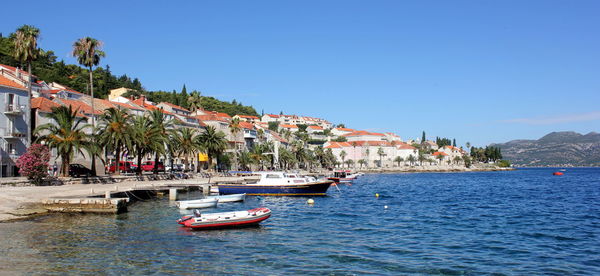 Boats moored on sea at harbor against clear blue sky