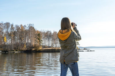 Young woman looking through binoculars at birds on lake birdwatching, ecology research nature