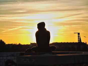 Rear view of silhouette man sitting against sky during sunset