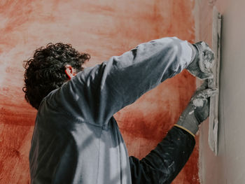 A young caucasian guy applies fresh putty with a large spatula on the wall