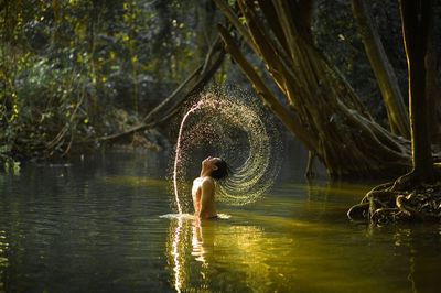 Shirtless man splashing water in lake against trees