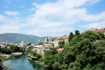 River amidst buildings and trees against sky