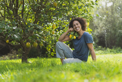 Smiling young woman sitting on grass against trees