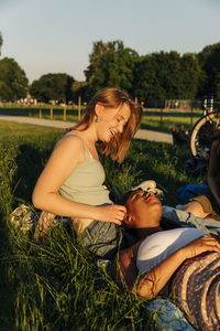 Smiling teenage girl talking with female friend lying on lap at park