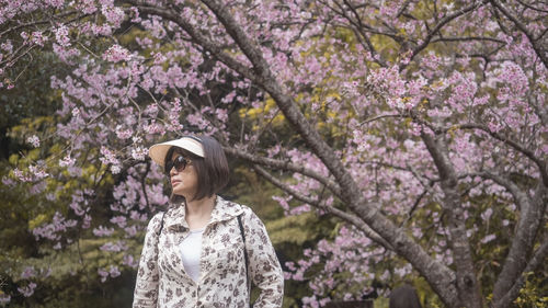 Portrait of young woman standing against cherry trees