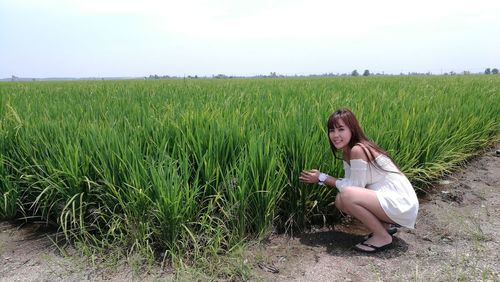 Woman crouching by crop on field