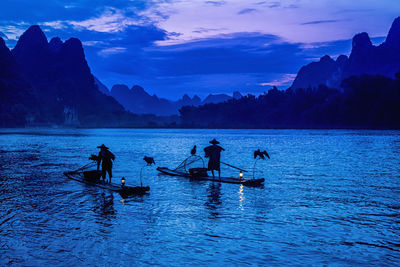 Men with birds on wooden raft in lake