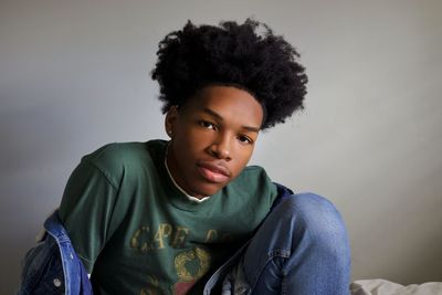 Portrait of young man sitting against wall at home