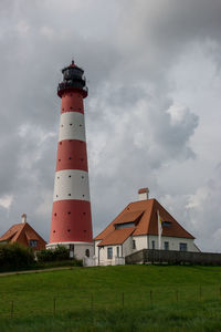 Lighthouse on field by building against sky