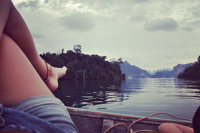 Low section of person sitting by swimming pool against lake