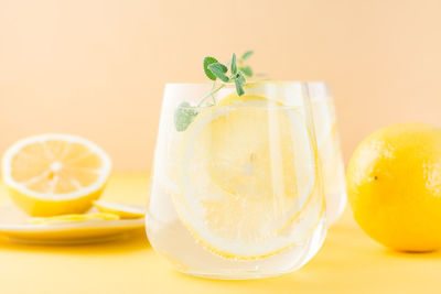 Sparkling water with lemon, melissa and ice in glasses and lemon slices on a saucer on a yellow 