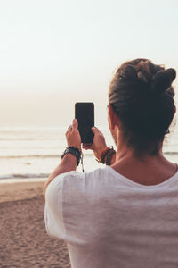 Rear view of woman photographing on beach