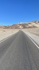 Road amidst desert against clear blue sky