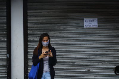 Young woman standing against wall texting