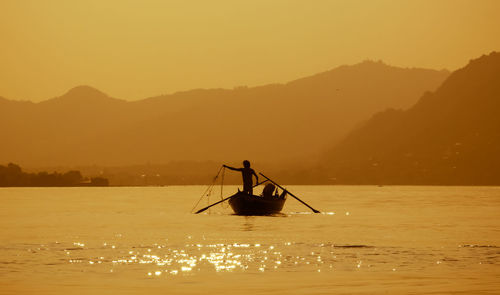 Silhouette boat in sea against orange sky