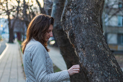 Side view of woman standing by tree trunk