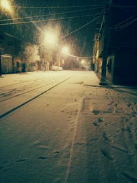 Snow covered illuminated road against sky at night