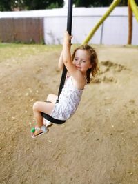 Full length of cute girl sitting while zip lining at playground