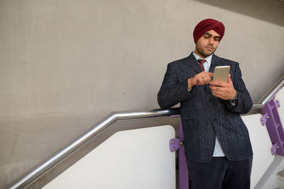 Young man using mobile phone while standing against wall