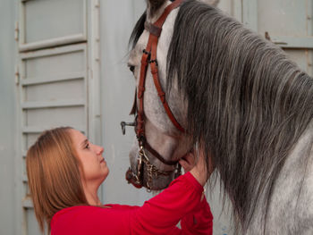 Young woman touching horse while standing metal built structure