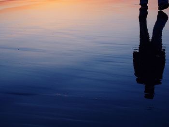 Low section of man standing on puddle at sunset