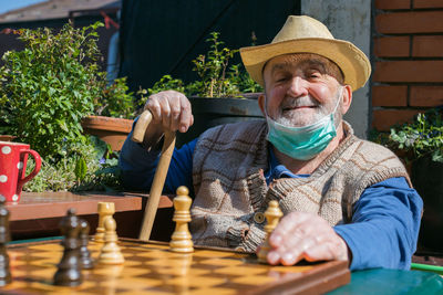 Portrait of senior man wearing mask playing chess while sitting outdoors