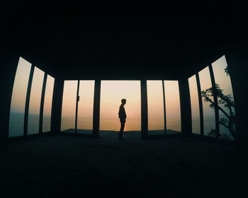 Silhouette man standing in built structure against sky during sunset