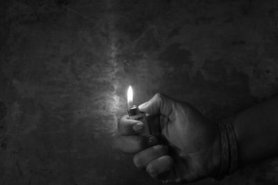 Cropped hand of person holding illuminated cigarette lighter against wall