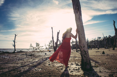 Portrait of woman standing by tree trunk against sky