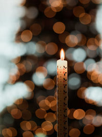 Close-up of candle burning against illuminated lights at night