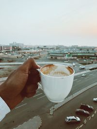 Close-up of hand holding coffee cup against cityscape