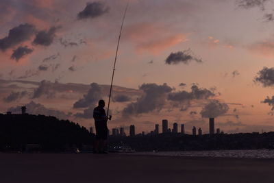 Silhouette man standing by cityscape against sky during sunset