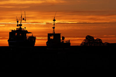 Silhouette ship on sea against orange sky