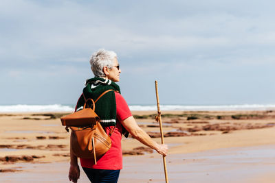 Man holding umbrella on beach against sky