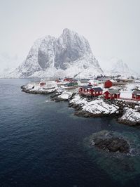 High angle view of houses by sea against snowcapped mountains and sky during winter
