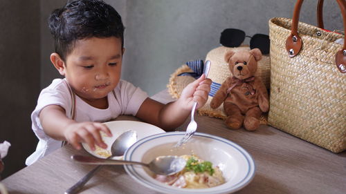 Baby boy eating food on table at home