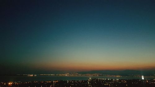 Illuminated cityscape by sea against sky at night