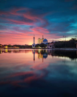 Reflection of factory on lake against sky during sunset