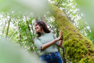 Smiling young woman standing by tree against plants