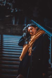 Portrait of young woman wearing warm clothing while standing on staircase at night