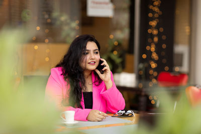 A smiling indian businesswoman talks on her mobile phone during a break in a cafe