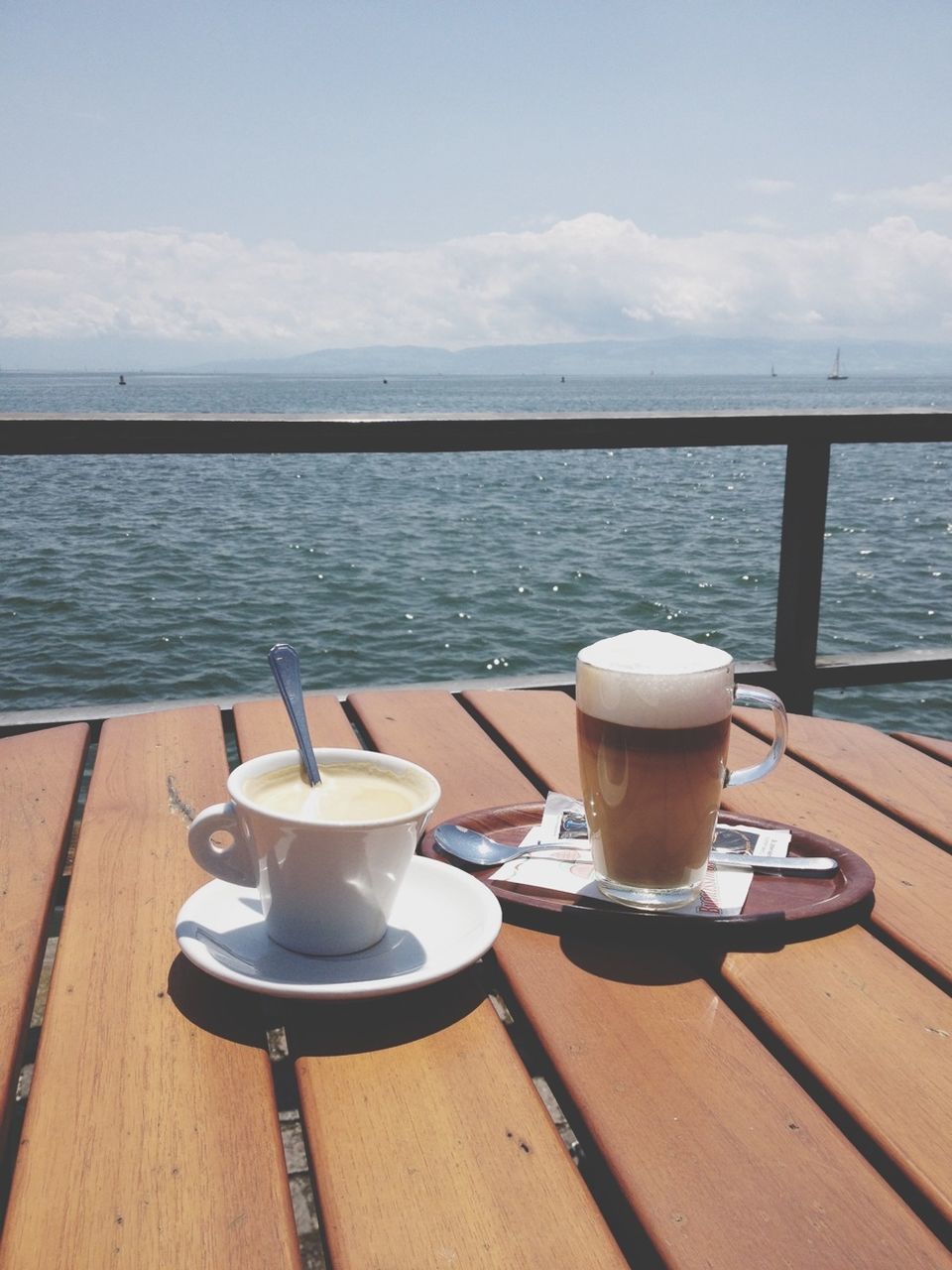 sea, table, water, drink, food and drink, sky, coffee cup, horizon over water, refreshment, coffee - drink, wood - material, saucer, day, chair, tranquil scene, still life, cloud, beach, sunlight, absence