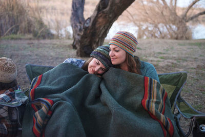 Affectionate female friends covered with blanket sitting at camp site