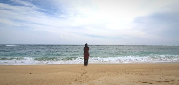 Rear view of man standing on beach against sky