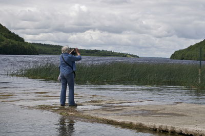 Rear view of man standing by sea against cloudy sky