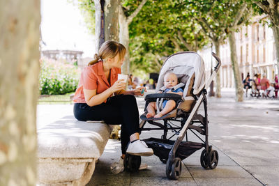 Portrait of young mother with her baby in a child carrier drinking a coffee while scrolling